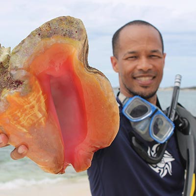Dr Ancilleno Davis on the beach holding a seashell towards the camera.